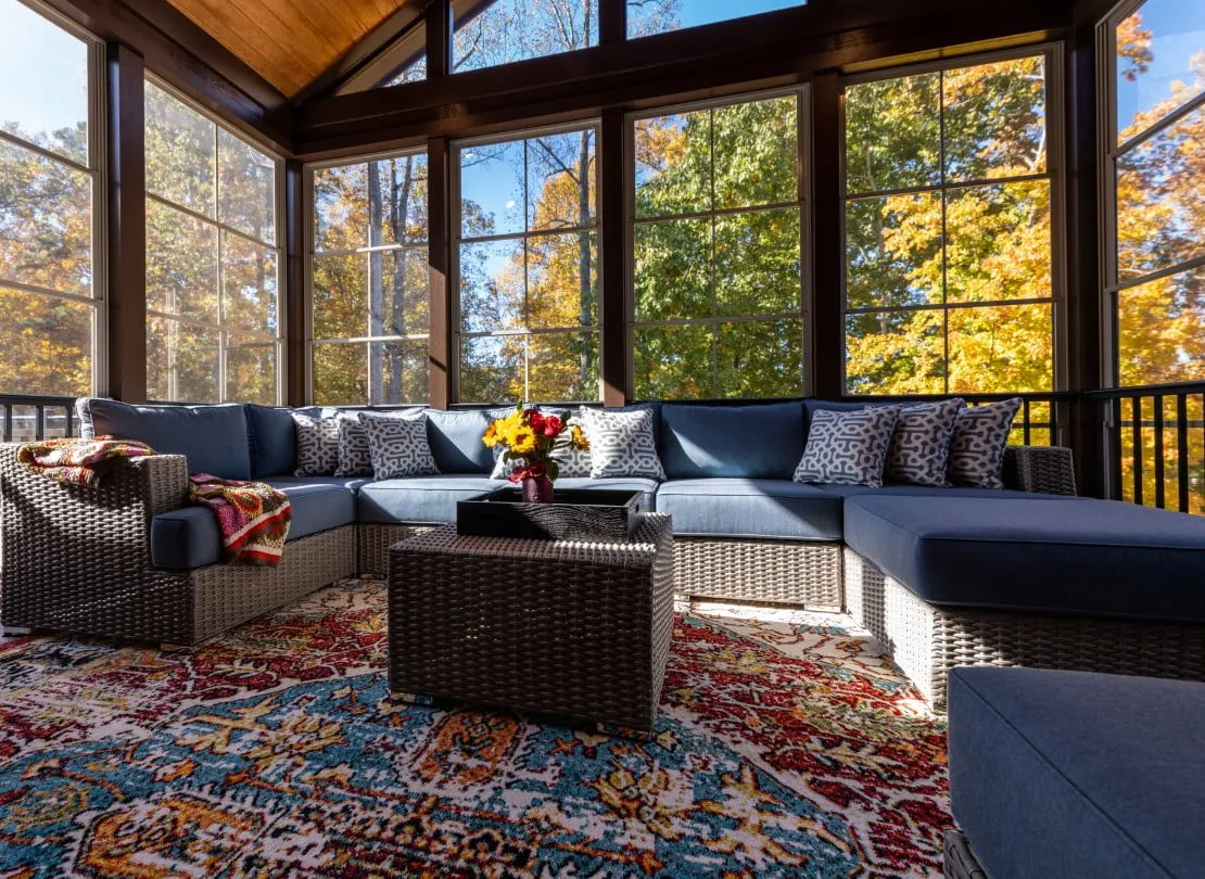 A sunroom with a couch and fall trees outside the windows