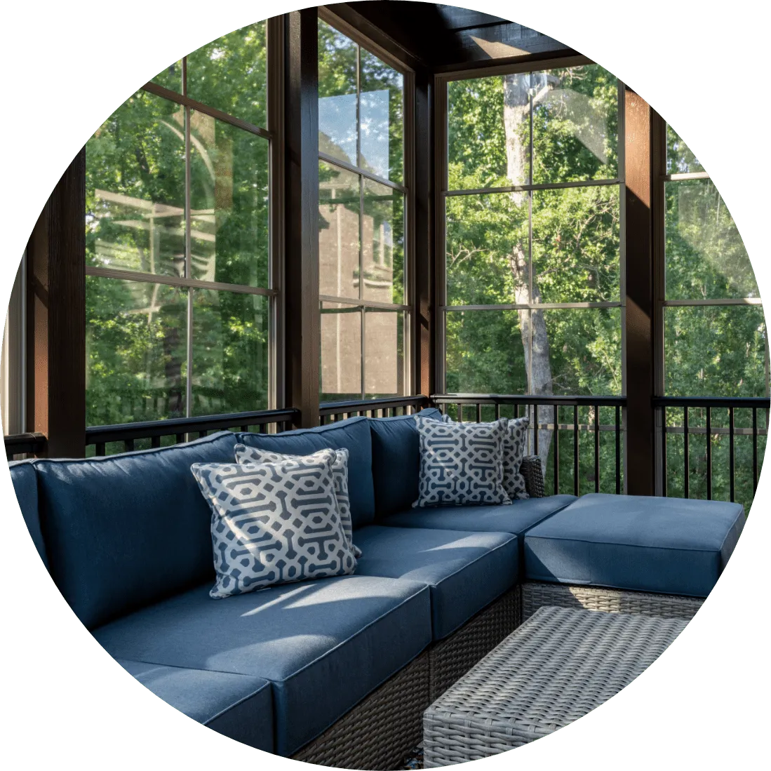 A sunroom with a couch and fall trees outside the windows